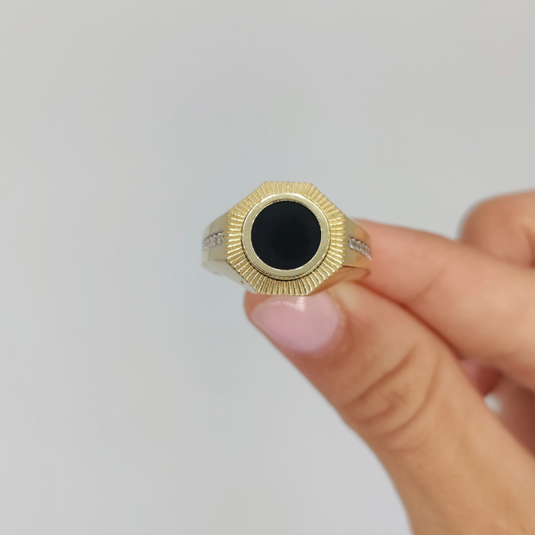 Un anillo de sello redondo con azabache y circonitas en los costados, elaborado en oro de 18 quilates, es una joya elegante y sofisticada