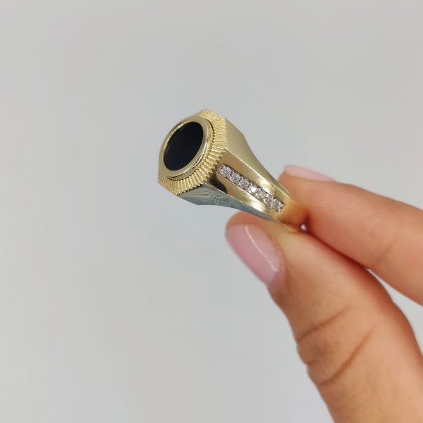 Un anillo de sello redondo con azabache y circonitas en los costados, elaborado en oro de 18 quilates, es una joya elegante y sofisticada