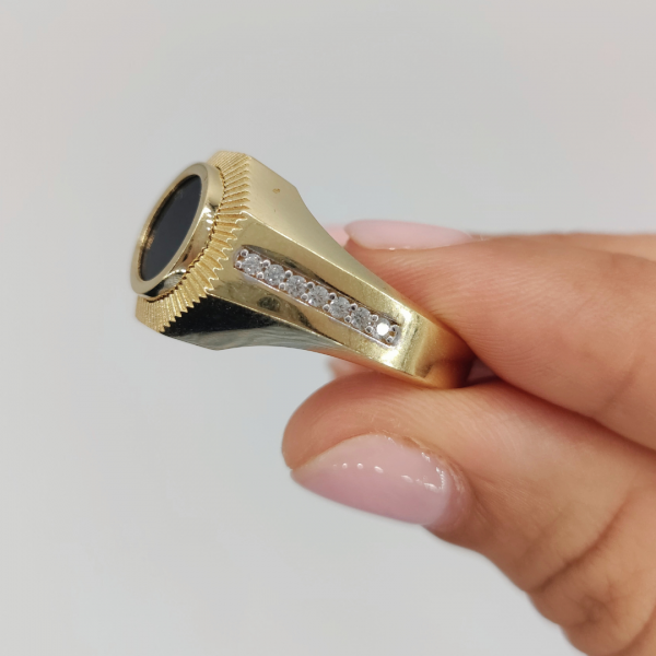 Un anillo de sello redondo con azabache y circonitas en los costados, elaborado en oro de 18 quilates, es una joya elegante y sofisticada