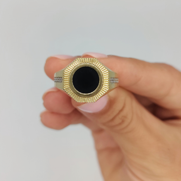 Un anillo de sello redondo con azabache y circonitas en los costados, elaborado en oro de 18 quilates, es una joya elegante y sofisticada