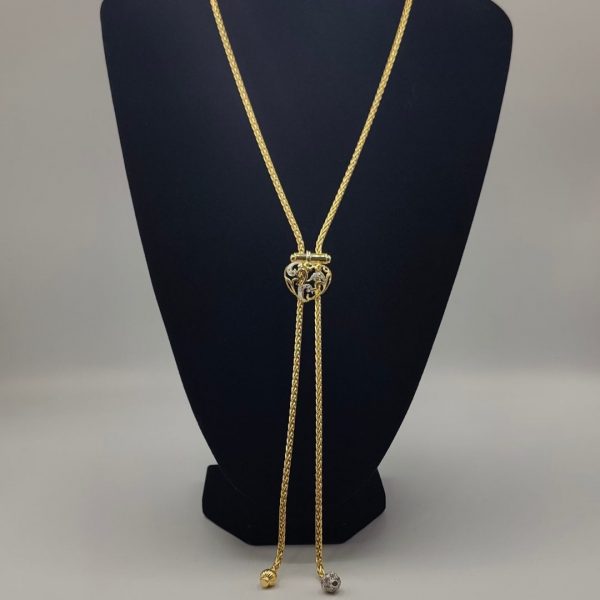 cadena estilo corbatín con eslabones tipo serpiente, cierre corazón con circonitas y el final de la cadena tiene dos borlas una de ellas lleva de circonitas