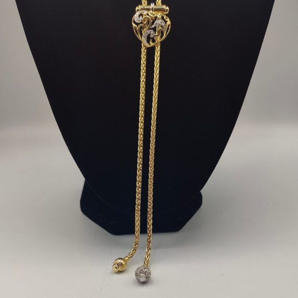 cadena estilo corbatín con eslabones tipo serpiente, cierre corazón con circonitas y el final de la cadena tiene dos borlas una de ellas lleva de circonitas