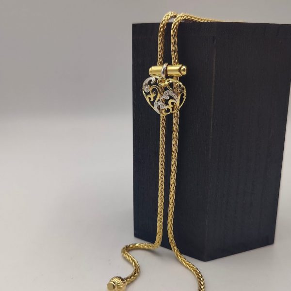 cadena estilo corbatín con eslabones tipo serpiente, cierre corazón con circonitas y el final de la cadena tiene dos borlas una de ellas lleva de circonitas